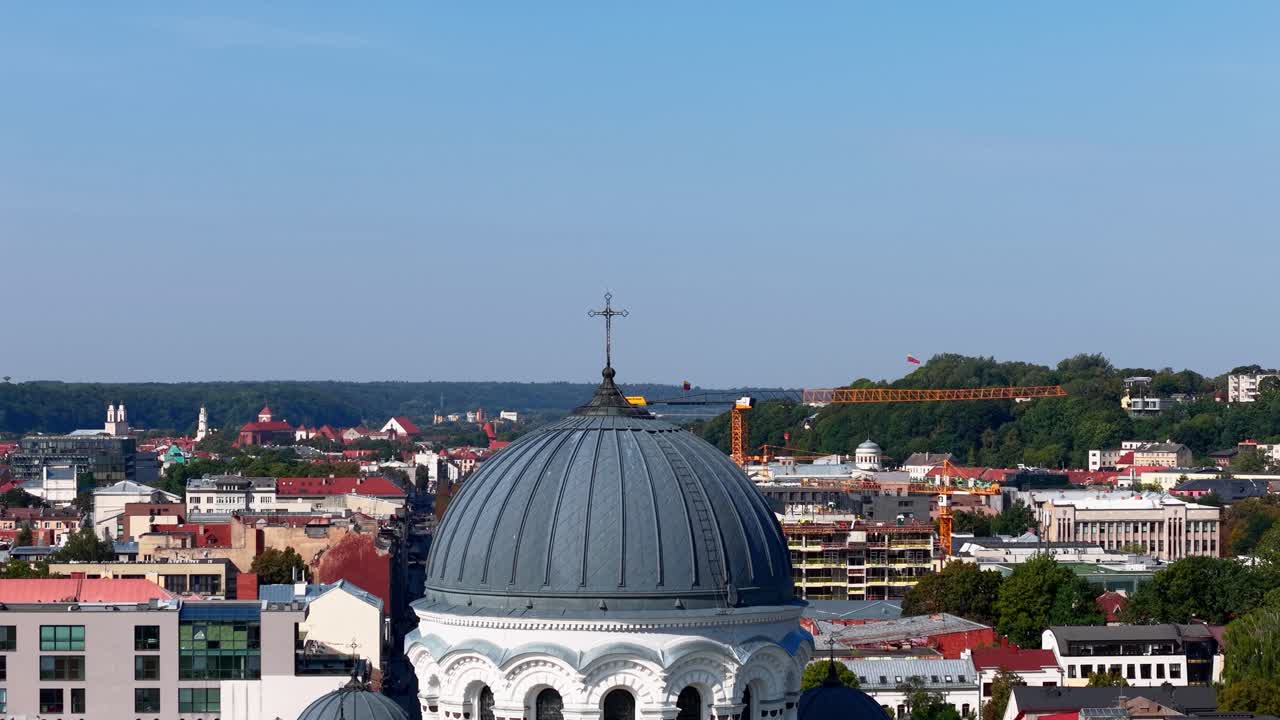 Close-up aerial view of the dome and cross of the St. Michael the Archangel Church in Kaunas, Lithuania, with the city skyline in the background under a clear blue sky