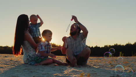 Junge-Eltern-Und-Zwei-Söhne-Der-Familie-Spielen-Mit-Seifenblasen-Bei-Sonnenuntergang