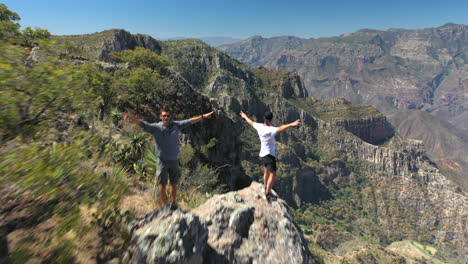 Tres-Hombres-Levantando-Los-Brazos-Y-Con-Vistas-A-La-Barranca-Del-Cobre,-México,-Antena-Delantera