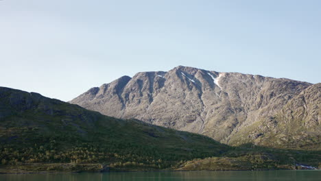 parallax effect of mountains behind green lake, early autumn sunny morning