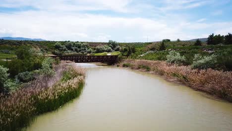 Drohnenschuss,-Der-Einen-Fluss-Hinauf-In-Richtung-Einer-Brücke-Auf-Einem-Golfplatz-Geht