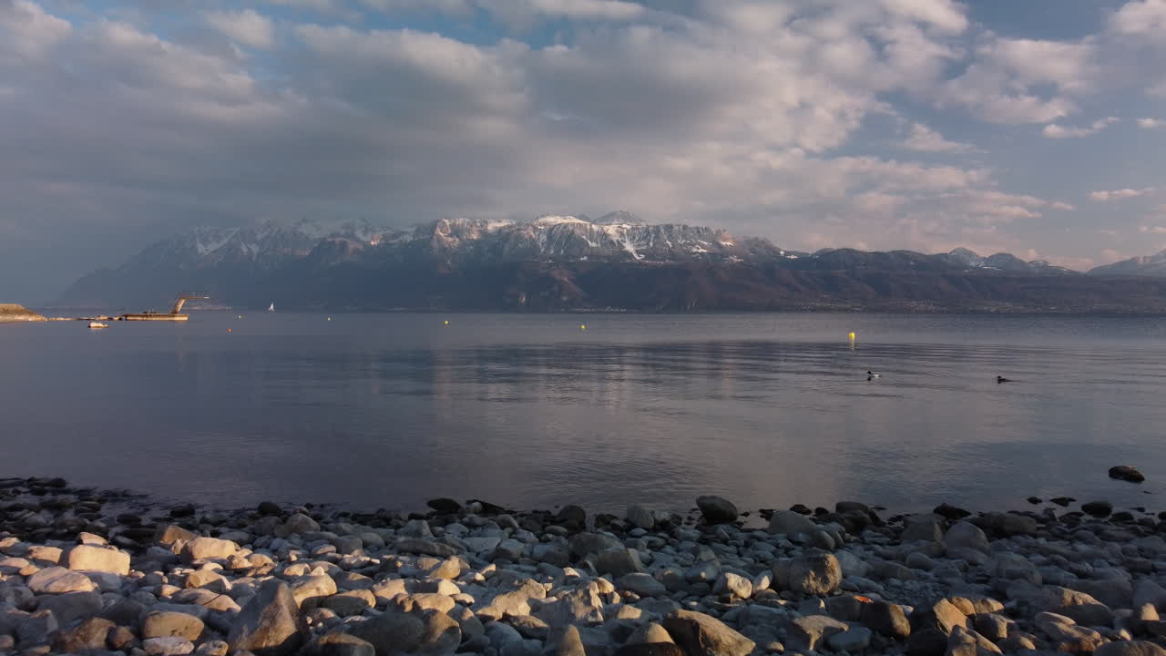 vuelo aéreo lento sobre la superficie del lago de ginebra con los alpes suizos en el fondo