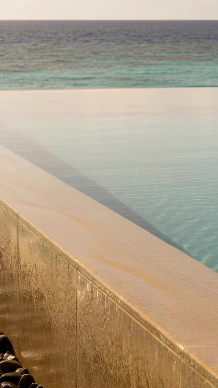 Vertical video: Spilling stone coping infinity edge cascading spillway at pool deck with dark rocks