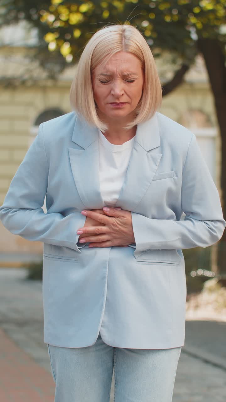 triste mujer de negocios caucásica madura que sufre de dolor de estómago mientras camina por la calle de la ciudad