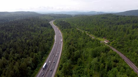 dynamic drone shot of national road and railroad next to each other in small european country leading the way through the belt of green trees and forest