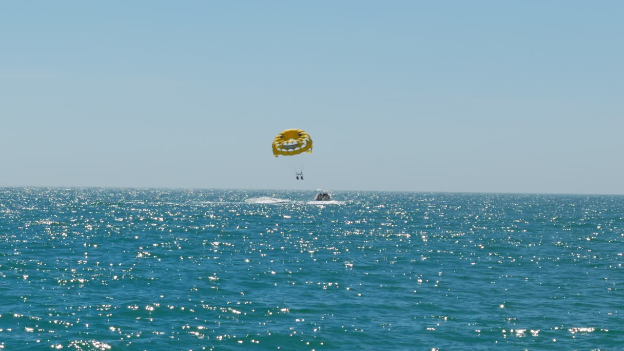 People beginning to go up parasailing and flying high above the turquoise Gulf of Mexico water
