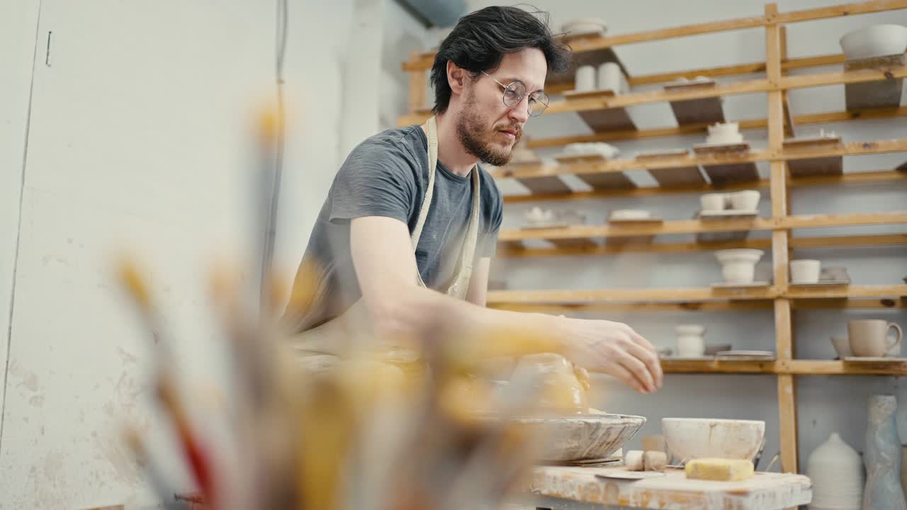 Tracking shot of male potter working on potter's wheel, sculpting ceramic crockery, slow motion