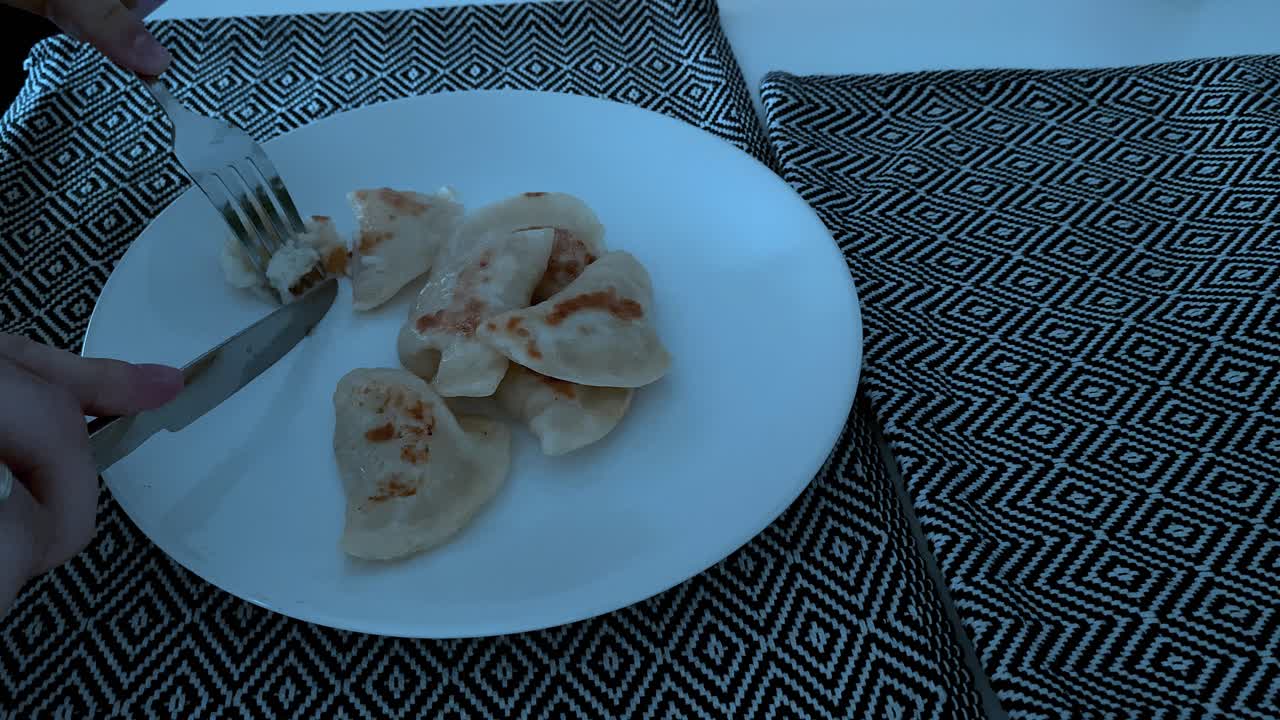 Close up, cutting dumplings with a knife on a white plate, under the plate a decorative pad in a fashionable pattern,