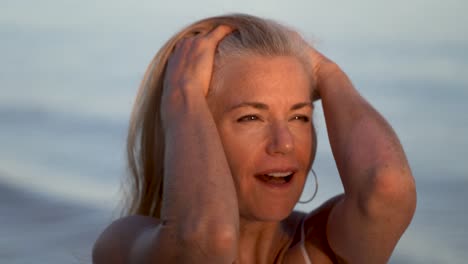 hermosa mujer madura mirando hacia otro lado y luego hacia el sol poniente y luciendo sorprendida, agarrando su cabello