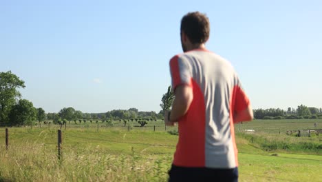 closeup of trail runner followed from behind on winter dyke passing dutch farmland river valley against a blue sky