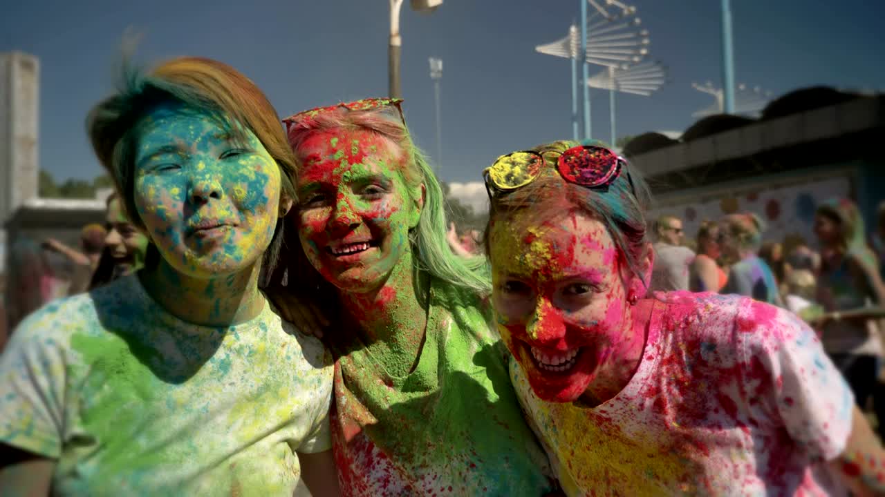 Three young multi-ethnic girlfriends are laughing on holi festival in daytime in summer, friendship concept, color concept