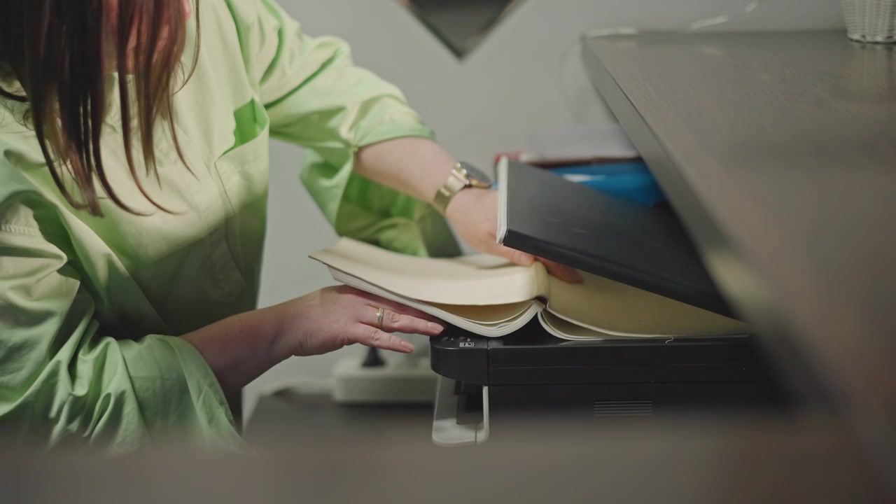 Copying sheet music at office printer, white teacher loads pages into copier, adjusting settings, closeup of hands feeding paper, organized studio atmosphere, focused methodical pace