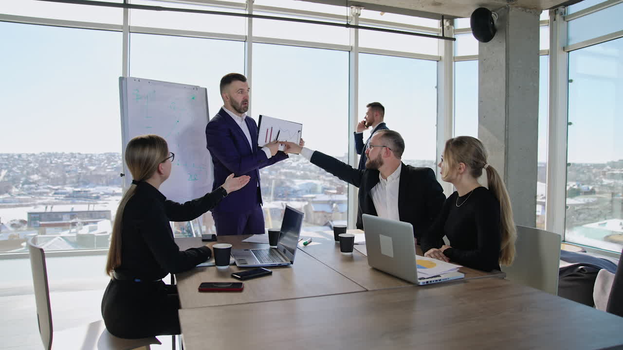 Coworkers' team discussing the chart in the hands of their chief. Active collaboration in the office atmosphere. Male businessman speaking on the phone at the backdrop.