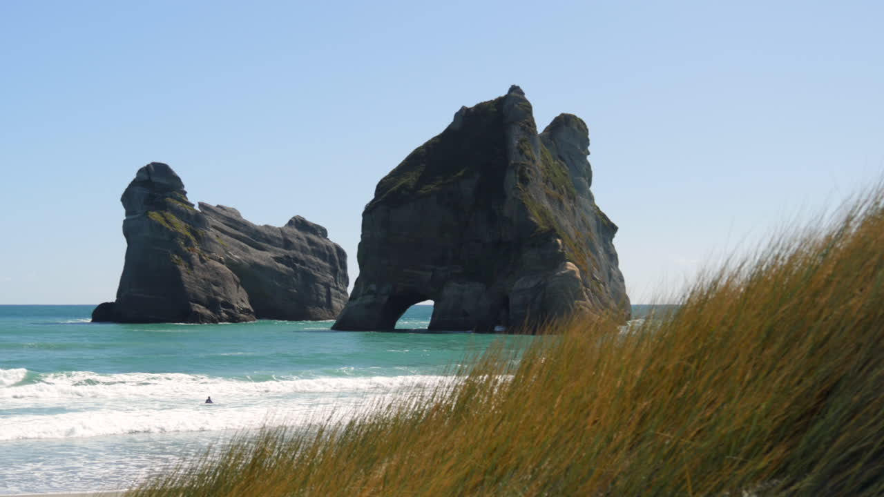Large sea stacks in shallow water near Whareriki Beach on New Zealand's South Island, tracking shot, right to left revealing rocks and beach.