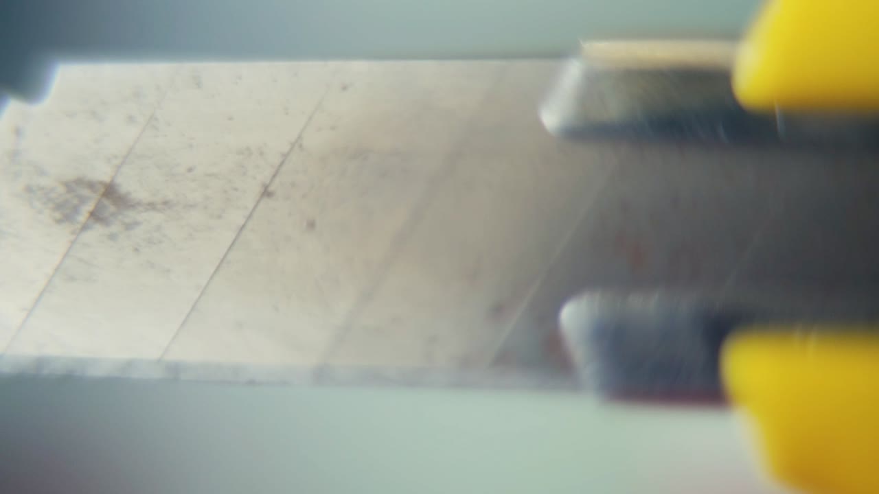 macro video de un cuchillo de utilidad, sacar la navaja de acero, cámara lenta 120 fps, agarre amarillo