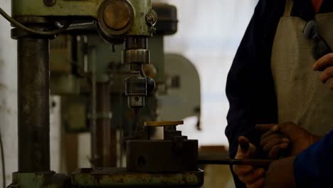 two metalsmith using drill press machine in workshop 4k