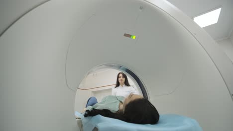 female patient is undergoing ct or mri scan under supervision of a radiologist in modern medical clinic. patient lying on a ct or mri scan bed, moving inside the machine.