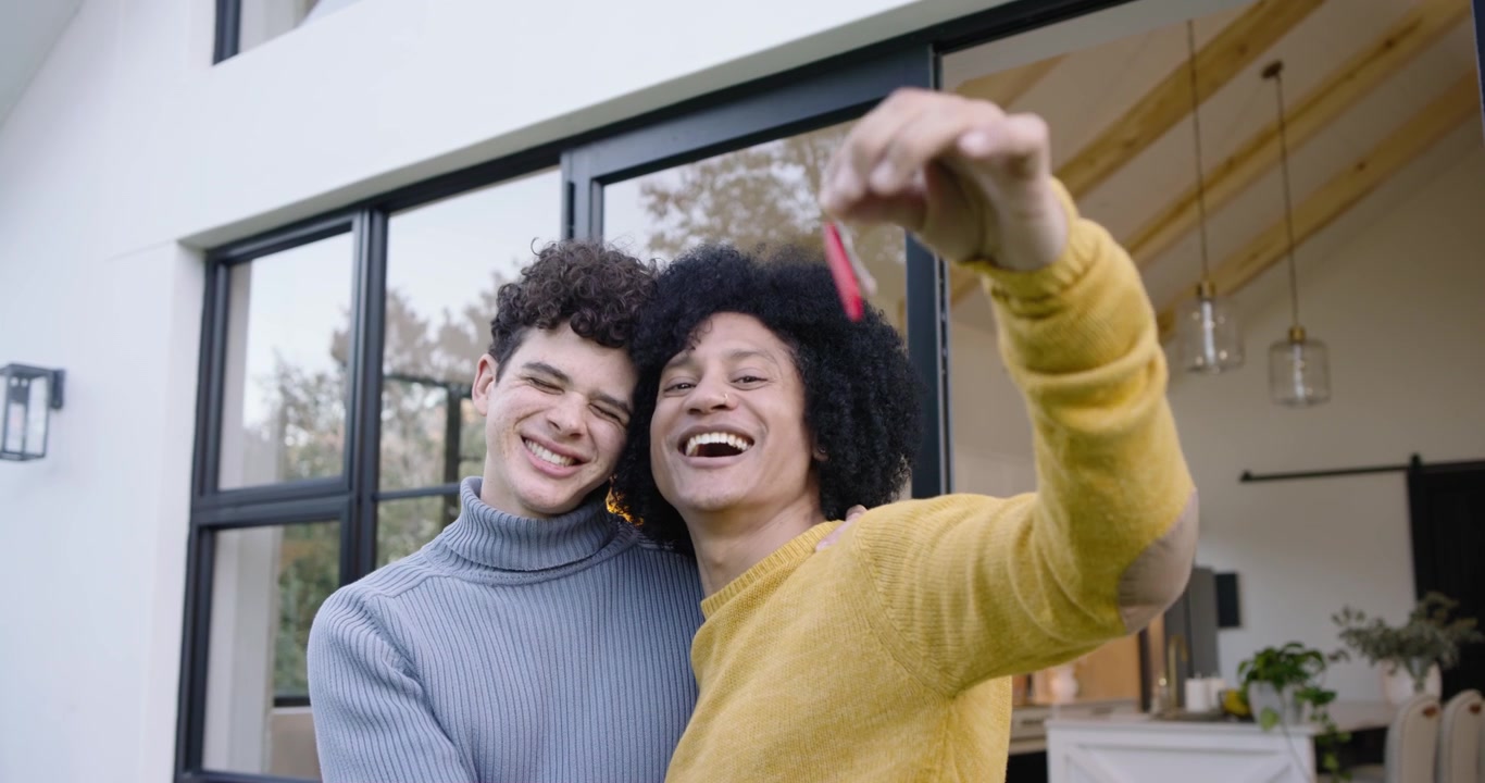 Pareja gay feliz sosteniendo las llaves de su nueva casa fuera de su hogar moderno