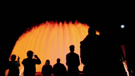 silhouettes of people who admire the high fountain with lights in barcelona