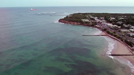 Umgekehrte-Luftaufnahmen-Mit-Blick-Auf-Den-Leuchtturm-Und-Point-Lonsdale,-Mit-Einem-Frachtschiff,-Das-In-Die-Bass-Strait,-Victoria,-Fährt