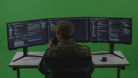 Back View Of Asian Man Soldier Developer Drinking Coffee And Using Computer To Write Code With Multiple Screens In Green Screen Studio