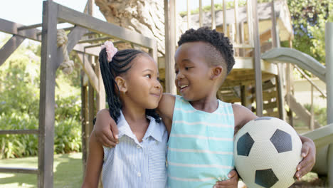 retrato de hermanos afroamericanos felices con fútbol en el jardín, en cámara lenta