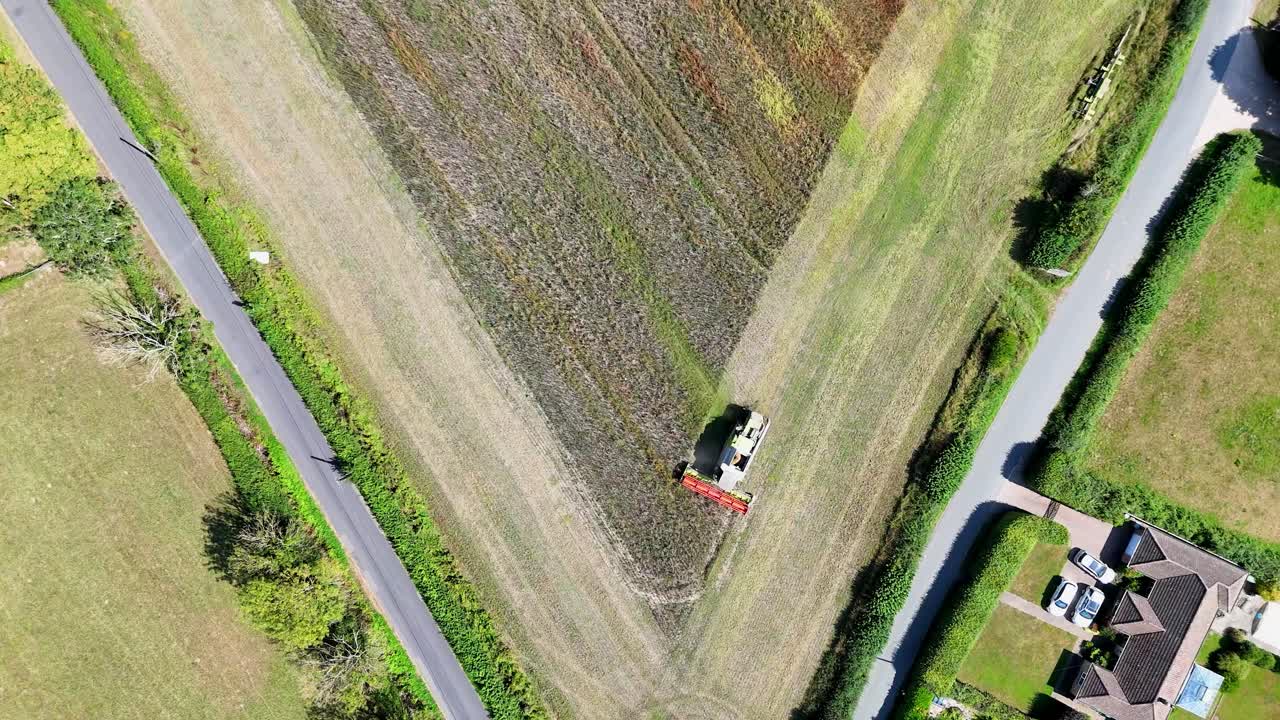 Cinematic birds-eye aerial of a combine harvester working farmland. Modern agriculture, contractors and farmers harvesting grain crops with efficiency from above