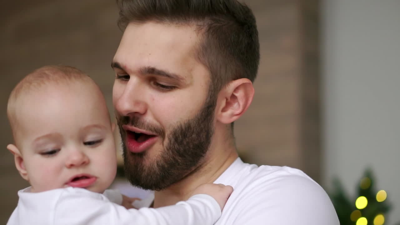 Bearded dad kissing baby. Close up of happy father with child on hands. Baby touching wrist watch on father hand.