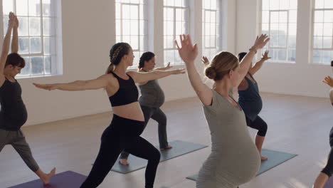 yoga class of young pregnant women practicing warrior pose enjoying healthy lifestyle group fitness workout in exercise studio at sunrise