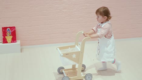 cute toddler baby girl pushing a toy cart in a play zone cafe