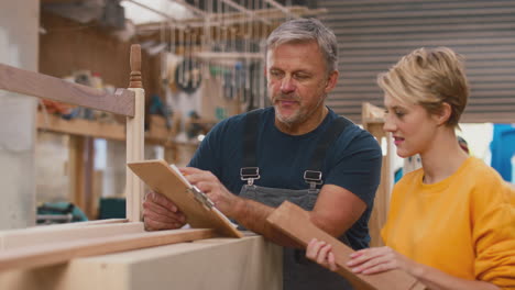 female apprentice learning skills from mature male carpenter in furniture workshop