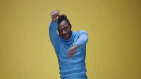 joyful man dancing in a blue turtleneck against a yellow background