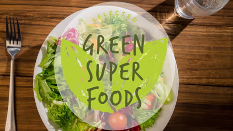 animation of green superfoods text in green over plate of fresh salad on wooden table