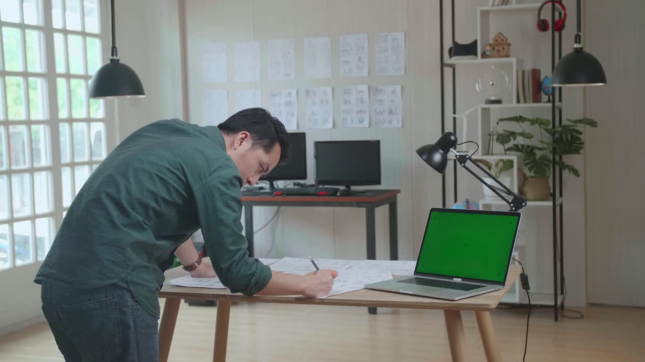 Asian Man Drawing Storyboard Animation Comic Cartoon With Mock Up Green Screen Laptop Computer, Design Creative Scene Layout At Studio. Behind Making Work Before Production Films Or Video Shot