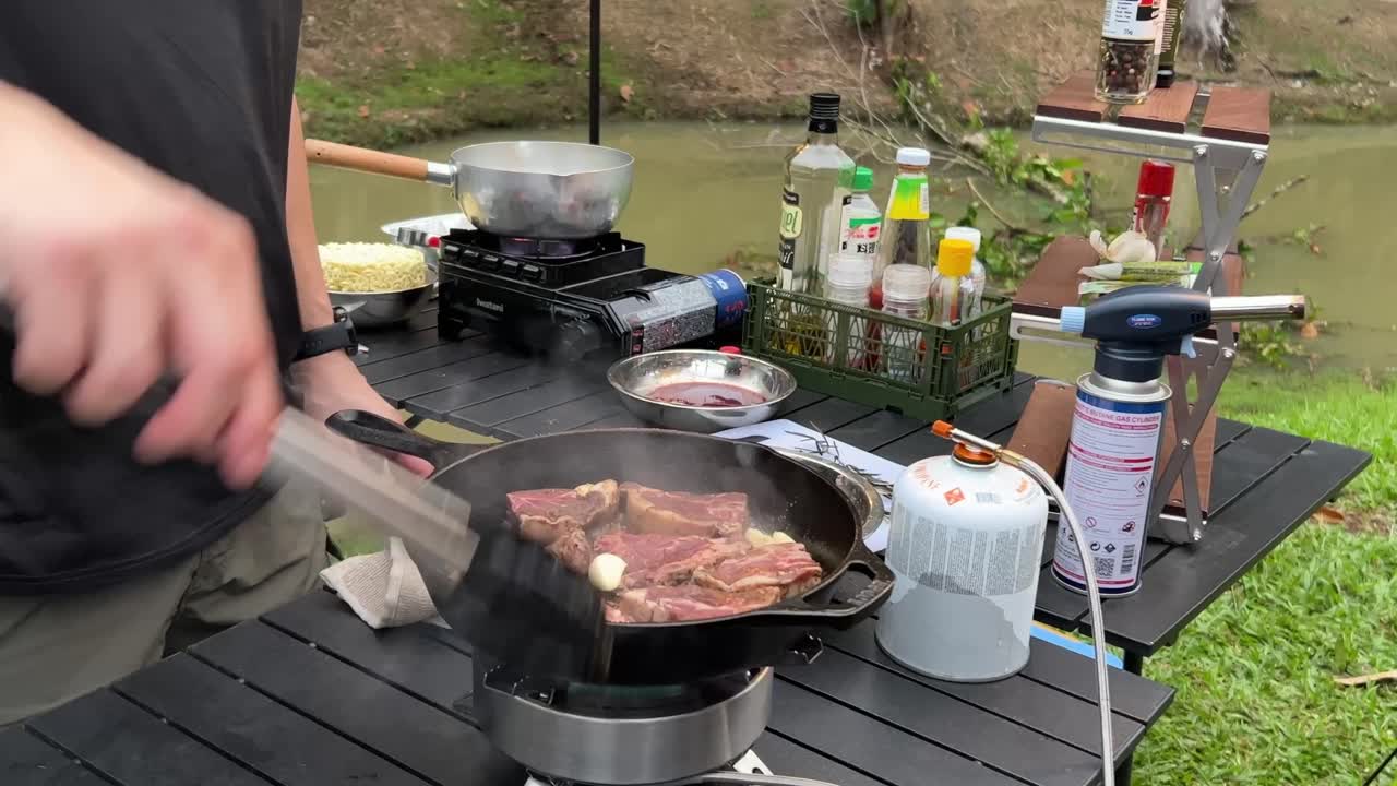 ambiente natural al aire libre, cocinando carne de res en una sartén de hierro fundido con fuego de estufa de portal, quemando, chisporroteando y cocinando con humos aromáticos en el campamento