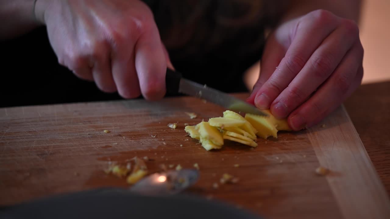 A stationary footage of a woman's hands while slicing peeled ginger using a knife on top of the counter