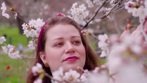 smiling woman touching delicate flowers of cherry blossoms in the botanical gardens of kyoto, japan