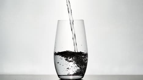 Slow‑motion close‑up of water pouring into a clear glass with bright white backlight