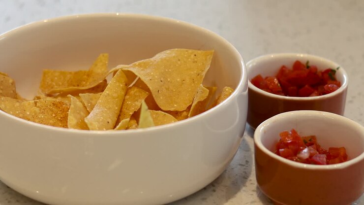 Hands serving salsa onto nacho chips in bowl