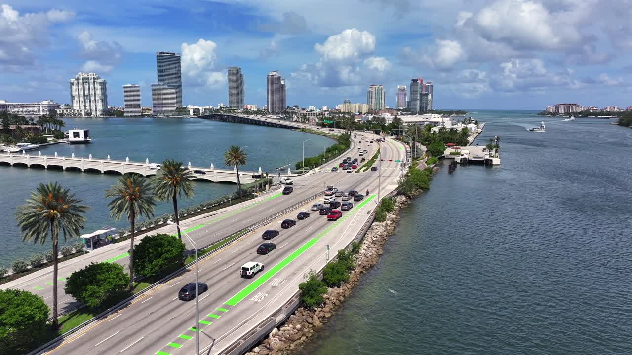 Drone flight over river bay in Miami with MacArthur Causeway and downtown in background. Sunny day in summer season. Traffic on road following to Skyscrapers. Wide shot
