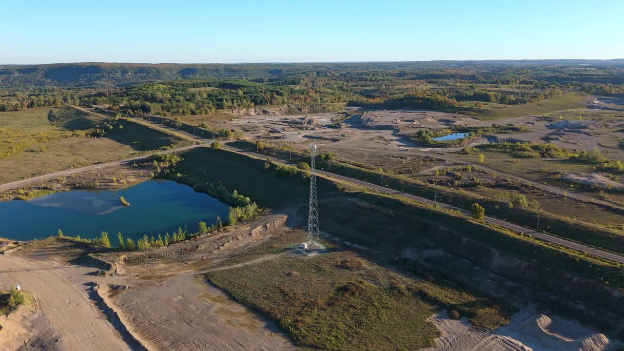 Drone shot flying forward toward a telecommunication tower surrounded by gravel pits, ponds, and open terrain in Caledon, Ontario, Canada