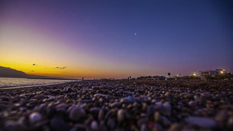 Nighttime-to-dawn-time-lapse-along-a-pebble-beach-in-Greece