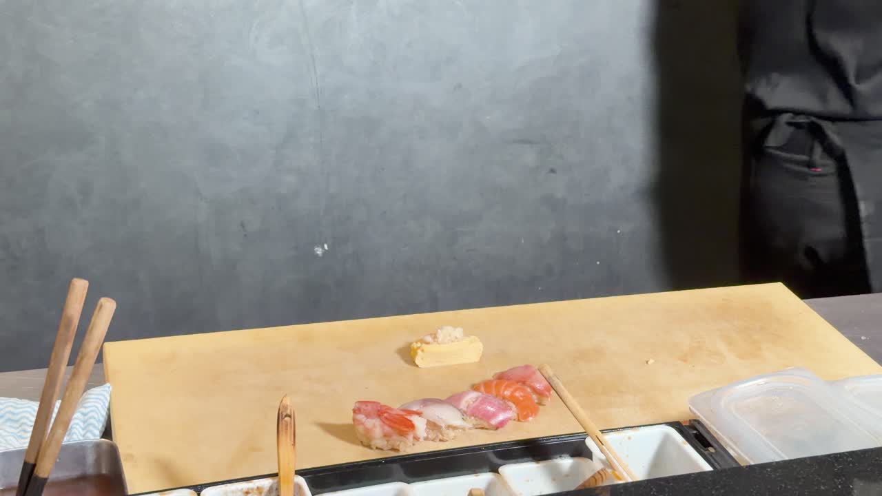 Profesionální sushi šéfkuchař aranžuje sashimi nigiri a tamago na dřevěném pultu, statický záběr zblízka