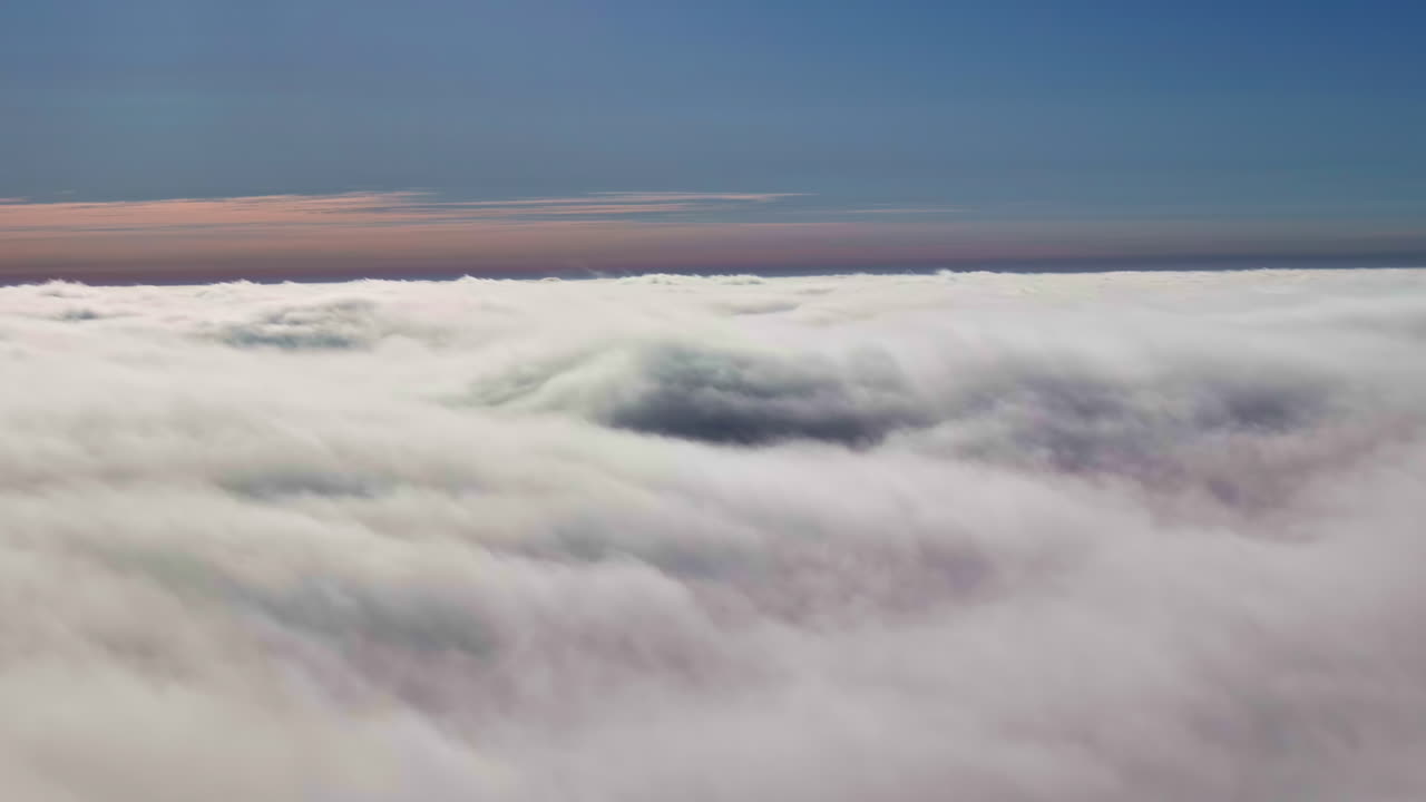 A view above the white fluffy clouds under a blue sky with a gray horizon in the distance