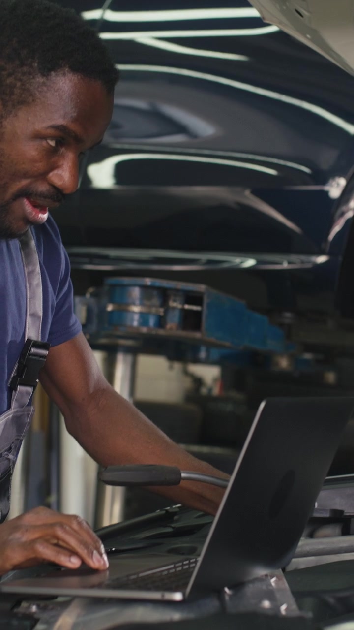 Meccanico d'auto moderno che utilizza un portatile per eseguire software diagnostico per la risoluzione dei problemi al motore.