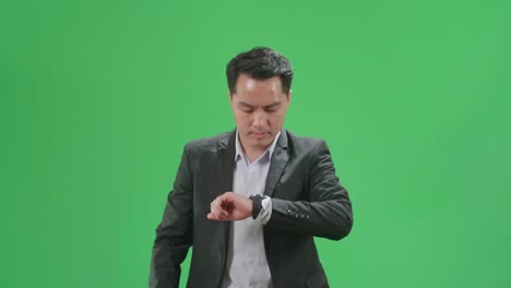 asian business man walking and looking at watch on green screen chroma key