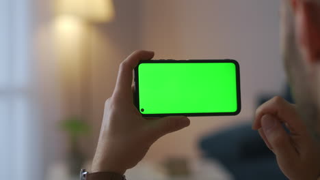 Der-Männliche-Benutzer-Verwendet-Eine-Neue-Anwendung-Im-Smartphone,-Das-Das-Gadget-Horizontal-Hält,-Und-Die-Greenscreen-Technologie-Für-Die-Montage-In-Nahaufnahme-Im-Innenbereich