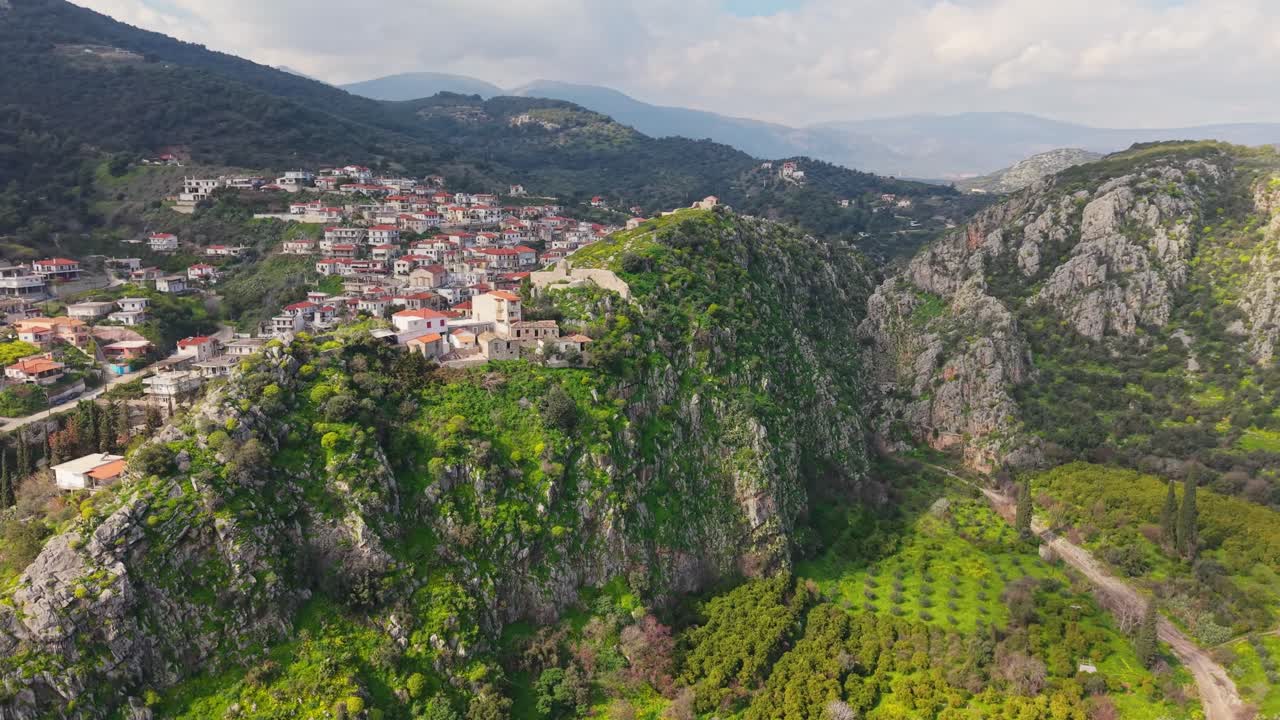 Drone ascends high to reveal a panoramic view of lush greenery, a deep gorge, and the picturesque village of New Epidavros nestled in the landscape