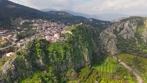 drone ascends high to reveal a panoramic view of lush greenery, a deep gorge, and the picturesque village of new epidavros nestled in the landscape