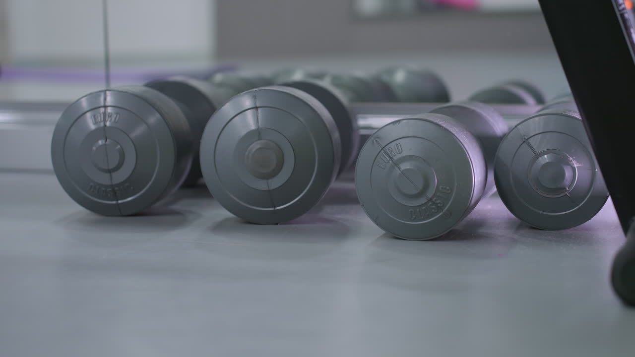 Close-up of multiple dumbbells neatly arranged on gym flooring, reflecting in a mirror, the setup highlights strength training equipment used for fitness workouts